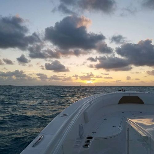 A boat sails toward the horizon over calm blue waters, sunset clouds glowing above a tranquil ocean.
