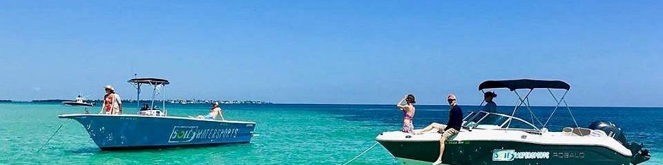 Two small tour boats float on clear turquoise water under a bright blue sky, with people relaxing onboard.